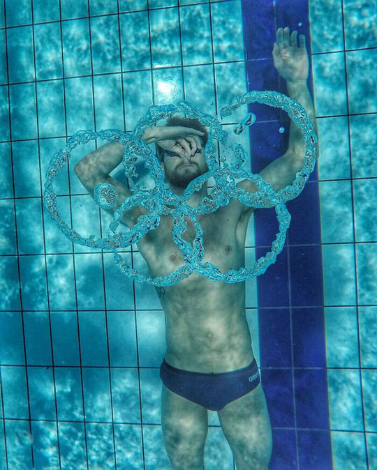 Một vận động viên bơi lội vẽ ra biểu tượng Olympic dưới nước bằng bóng khí.