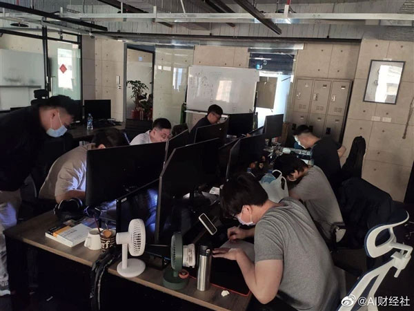 Cảnh dàn nhân viên đang đang đắm mình trong việc lập trình bằng bút và giấy dưới ánh đèn flash của điện thoại di động.