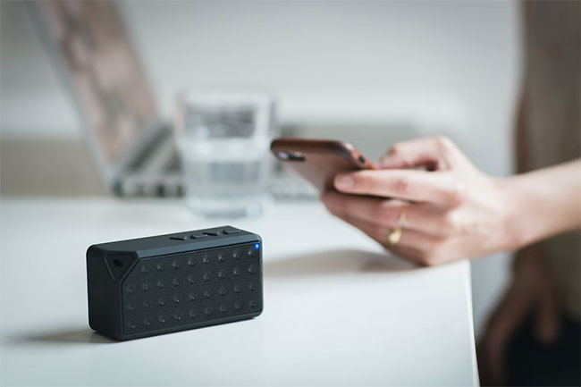 Người cầm Iphone bên cạnh loa di động màu đen