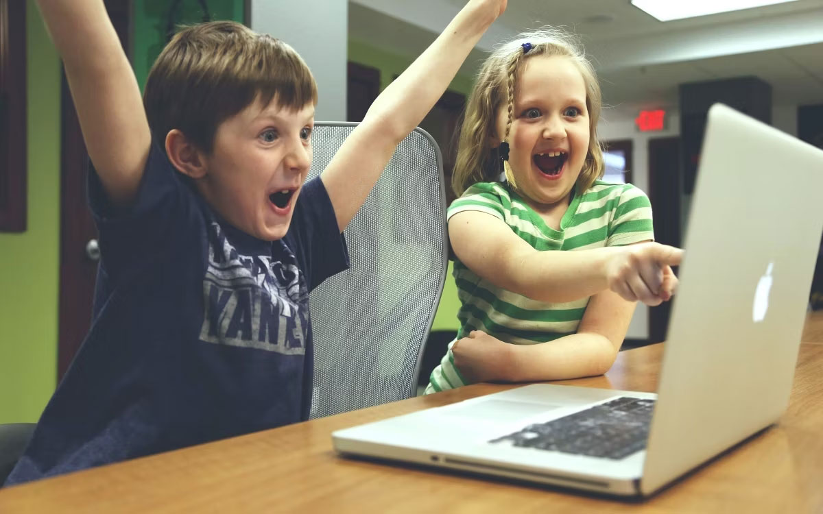 Hai đứa trẻ đang cười khi nhìn vào máy tính xách tay