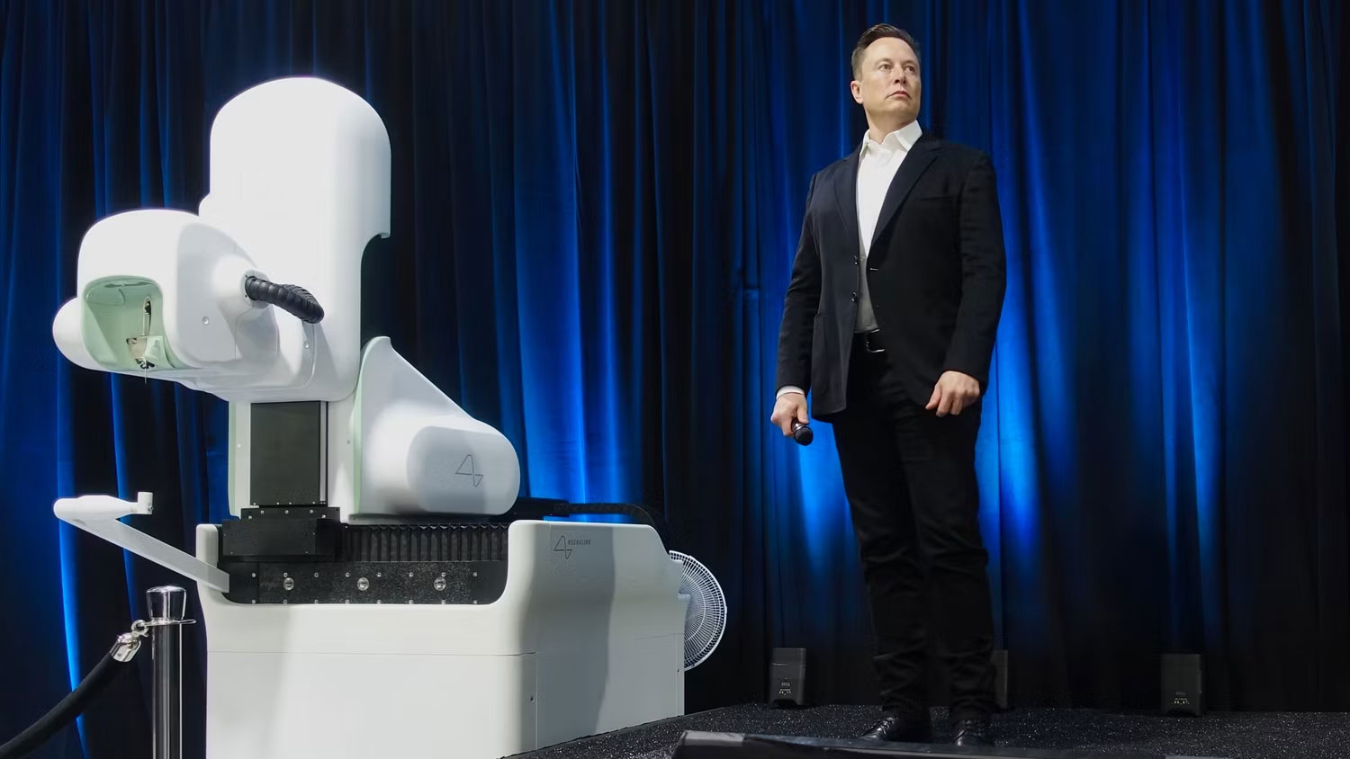 Elon Musk trên sân khấu bên cạnh máy Neuralink 