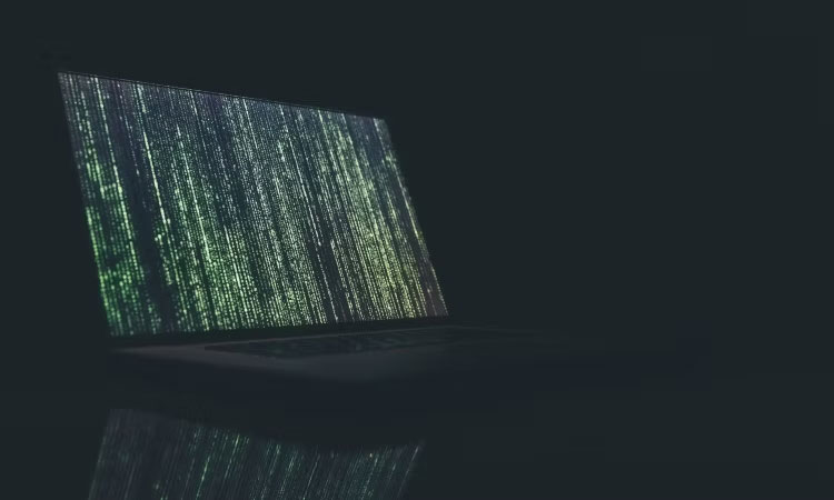 Một chiếc laptop màu xám trên nền tối với dòng chữ màu xanh lá cây chạy dọc màn hình
