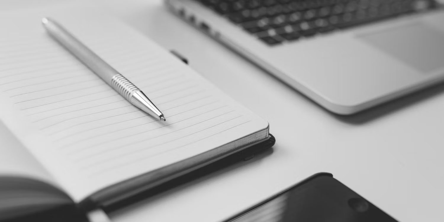 Cây bút bạc trên cuốn sổ bên cạnh chiếc laptop