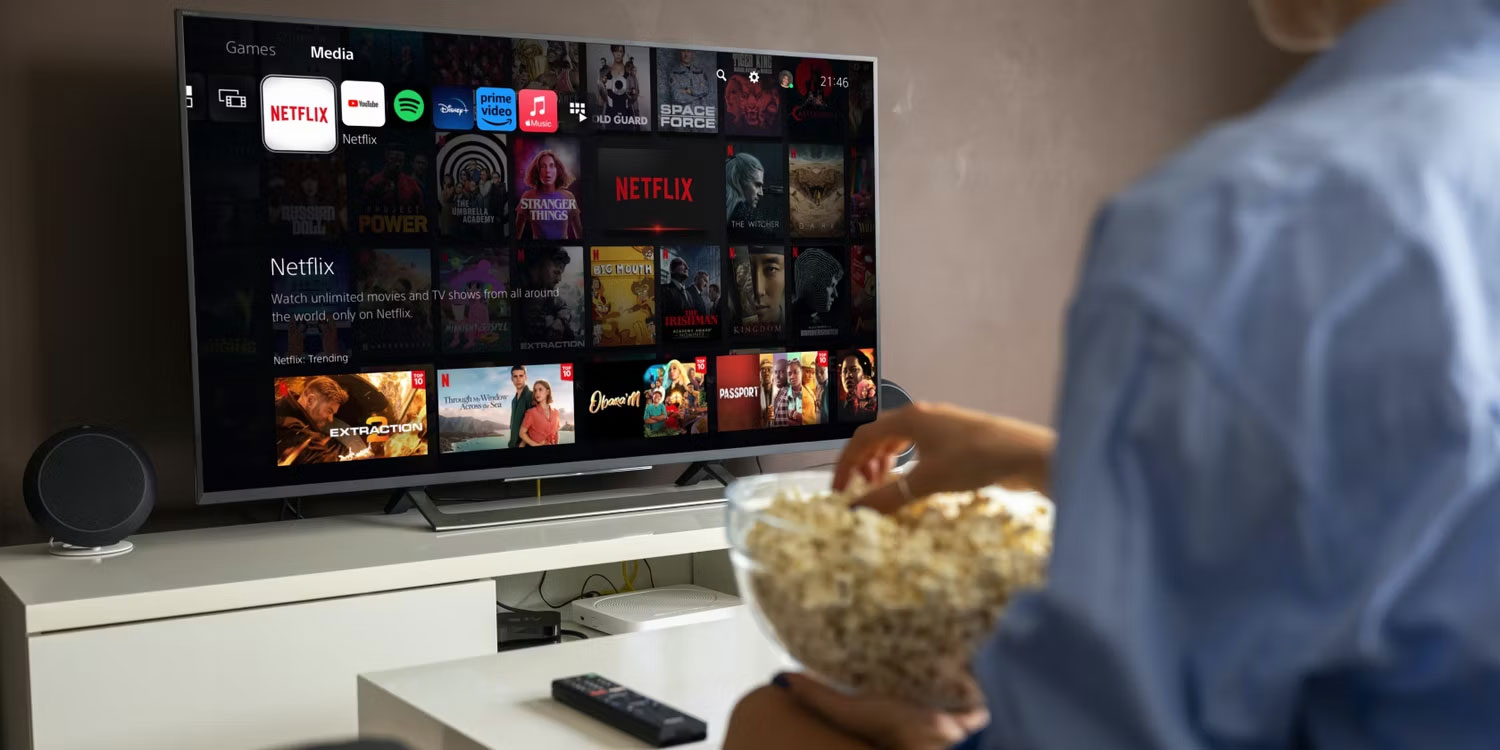 Một người phụ nữ cầm bỏng ngô đang ngồi trước TV thông minh với PS5 Netflix trên màn hình
