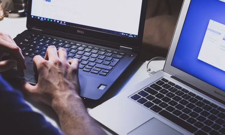 Một người đàn ông đang làm việc trên chiếc máy tính xách tay Dell màu đen bên cạnh chiếc MacBook Air màu bạc