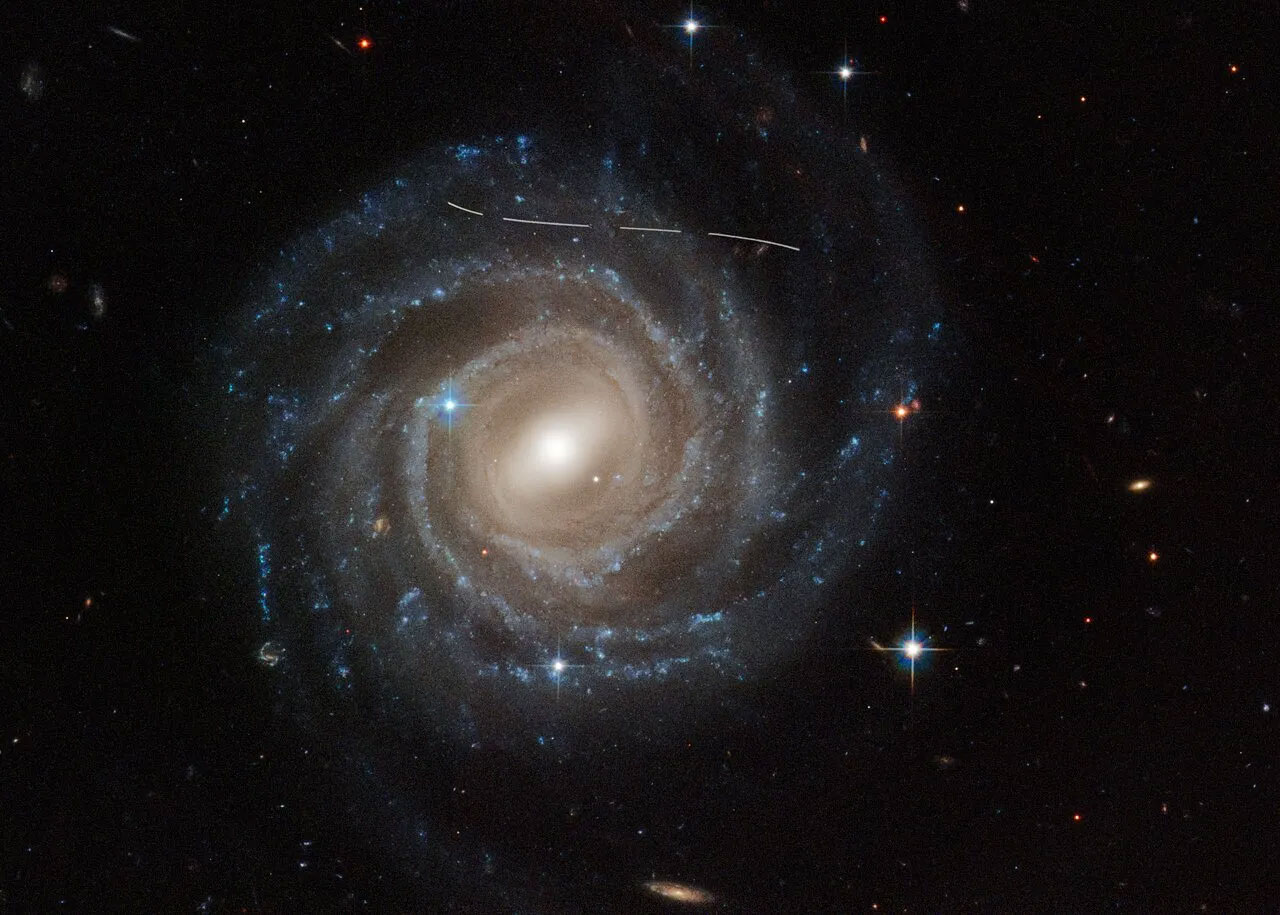 Hình ảnh từ Kính viễn vọng Không gian Hubble của NASA/ESA về thiên hà xoắn ốc có rào chắn UGC 12158 trông giống như ai đó đã lấy bút đánh dấu màu trắng vào. Trên thực tế, nó là sự kết hợp giữa độ phơi sáng theo thời gian của một tiểu hành tinh ở tiền cảnh di chuyển qua trường nhìn của Hubble, gây gián đoạn quá trình quan sát thiên hà. Một số ảnh phơi sáng của thiên hà đã được chụp, điều này được chứng minh bằng họa tiết nét đứt.