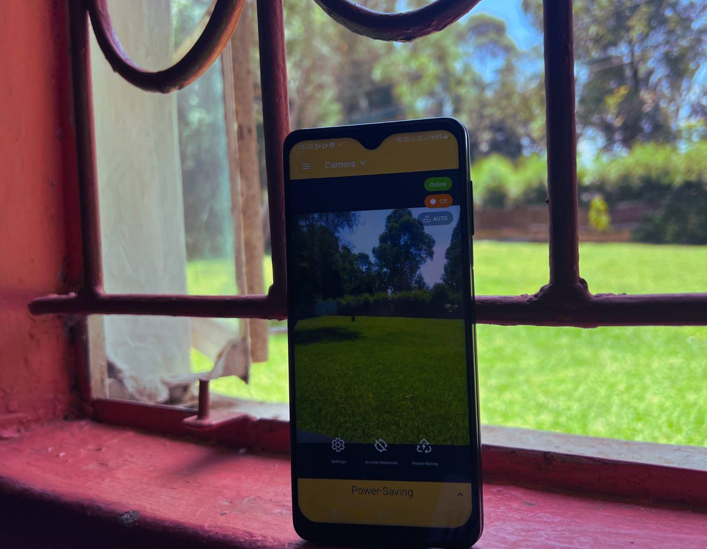 Điện thoại đặt trên ghế đẩu cạnh cửa sổ, chạy ứng dụng AlfredCamera, hoạt động như một camera an ninh